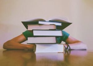 Schreibtisch mit Student, der sich hinter Bücherstapel verkriecht